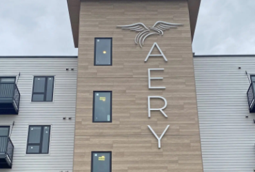 Equity Investments Featured Multifamily - Modern apartment building with wood-paneled center and “AERY” logo featuring a bird with outstretched wings.